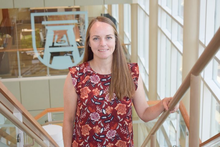 Woman in with pink, orange and white flowers standing on staircase in front of Augusta University logo.