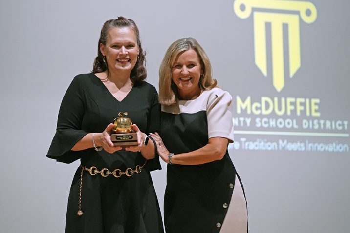 Two women smiling while one holds a trophy