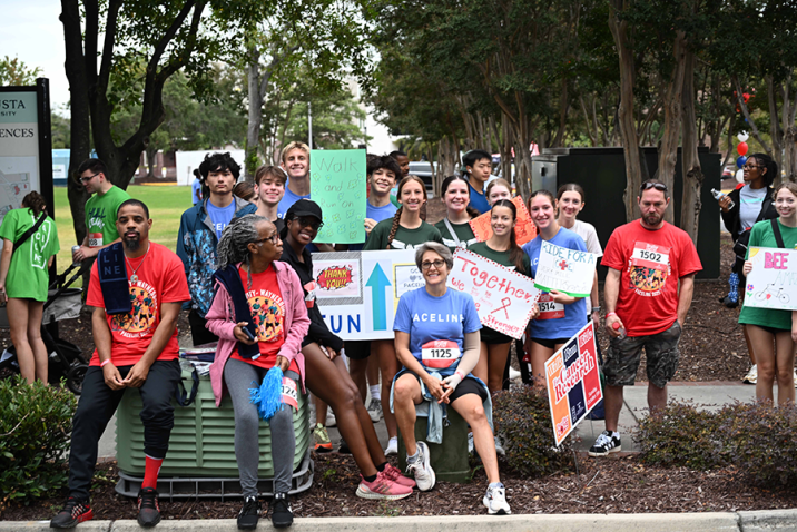 A large group of people hold signs and cheer as cyclists ride by during a race.